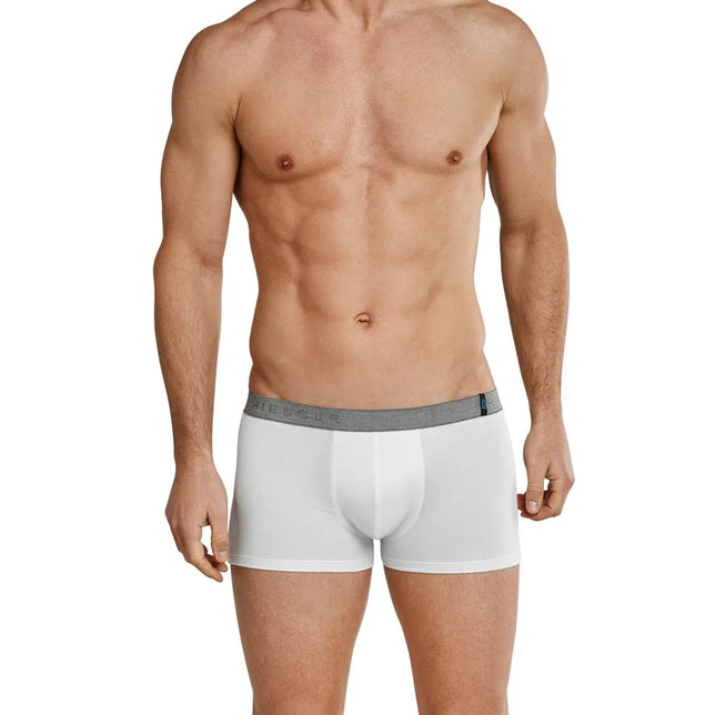 Model draagt een witte Schiesser herenboxer met lage taille, grijze logoband en aansluitende korte pijpen. - Jambelles