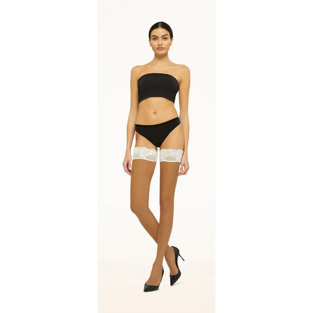Model draagt Wolford Nude 8 Lace stay-up kousen in huidkleur, transparant met brede witte kanten boorden. - Jambelles