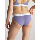 Model draagt paarse Calvin Klein dames bikinislip 0000F3787E met witte logoband en bijpassende bralette. - Jambelles