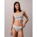 Model draagt een grijze Calvin Klein dames string thong met witte elastische logoband en bijpassende bralette. - Jambelles