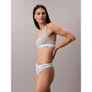 Model draagt een grijze Calvin Klein dames string thong met witte elastische logoband en bijpassende bralette. - Jambelles