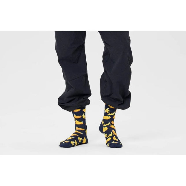 Happy Socks Banana BAN01 fantasiesokken voor dames en heren, donkerblauw met gele bananen, gedragen met zwarte broek. - Jambelles