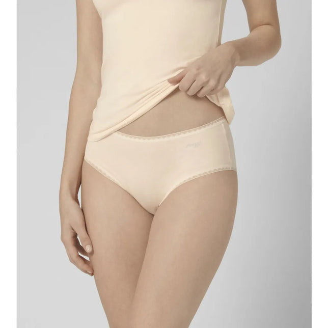 Model draagt een lichtbeige sloggi GO Midi damesslip met geschulpte boorden en subtiel logo voorop. - Jambelles