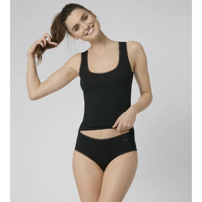 Model draagt een zwarte sloggi GO Midi damesslip met hoge taille en fijne kanten randjes, gecombineerd met een zwarte top. - Jambelles