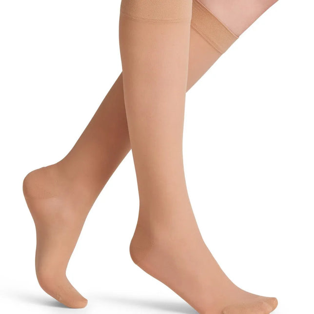 Falke Energize Kneehigh 30 dameskniekousen in huidkleur, transparant met brede boord, gedragen op gekruiste benen. - Jambelles