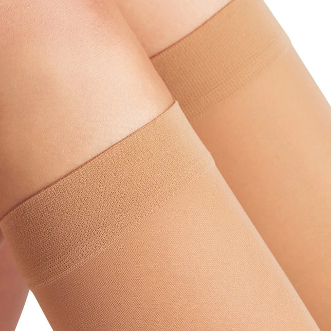 Falke dameskniekousen Energize Kneehigh 30 in huidkleur, gedragen op de benen, met brede boorden en transparante finish. - Jambelles