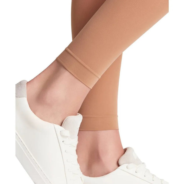 Falke damespanty Matt Deluxe 30 in huidkleur, met matte finish en voetloos model, gedragen met witte sneakers. - Jambelles