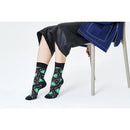 Happy Socks Christmas Night sokken in zwart met groene kerstbomen en kleurrijke stippen, gedragen door een zittend model. - Jambelles