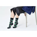 Happy Socks Christmas Night sokken in zwart met groene kerstbomen en kleurrijke stippen, gedragen door een zittend model. - Jambelles