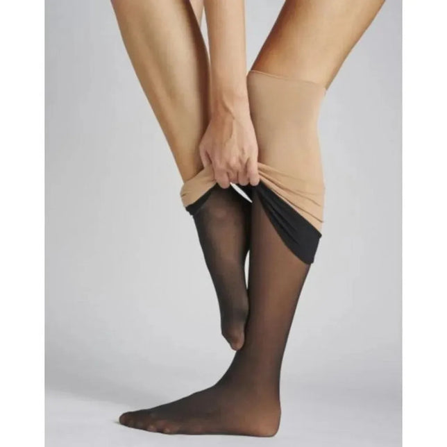 Model trekt de zwarte, transparante Hudson Dames Panty Thermo 120015729 aan onder een beige rok. - Jambelles
