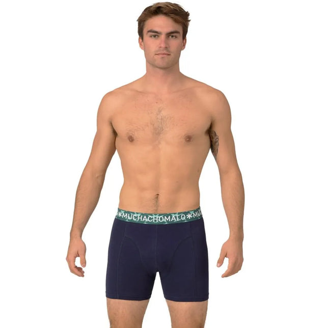 Model draagt een donkerblauwe Muchachomalo herenboxer met korte pijpen en een groene logoband. - Jambelles