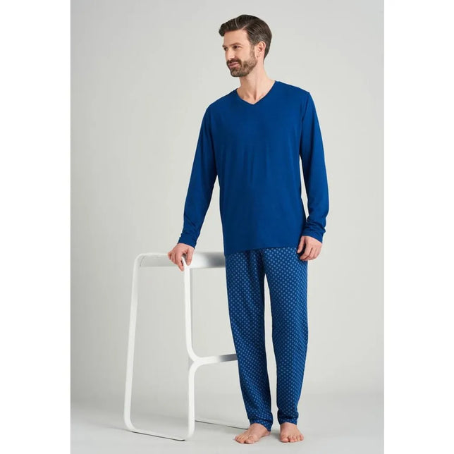 Model in blauw Schiesser heren nachtshirt 163846 met lange mouwen en V-hals, gecombineerd met een dessinbroek. - Jambelles