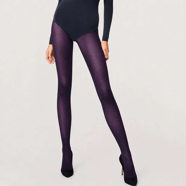 Model draagt Wolford Travel Leg Support panty 14622 in donkerpaars met subtiel diagonaal patroon en zwarte pumps. - Jambelles